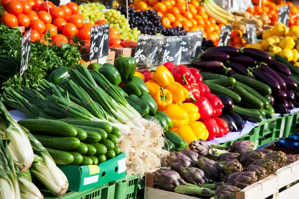 Banco di mercato con cassette di pomodori, peperoni, zucchine, cetrioli, melanzane e carciofi